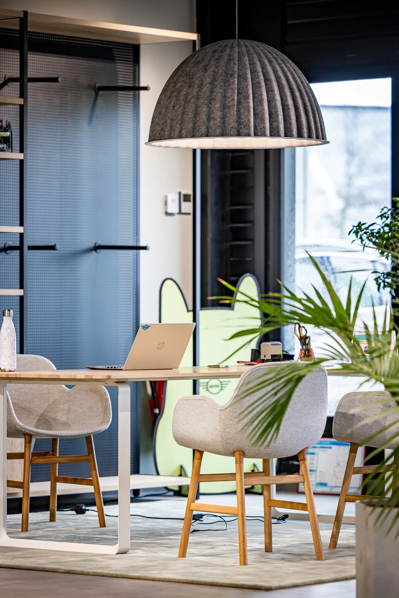 Espace de travail moderne avec table en bois, chaises grises, ordinateur portable et grande lampe suspendue grise