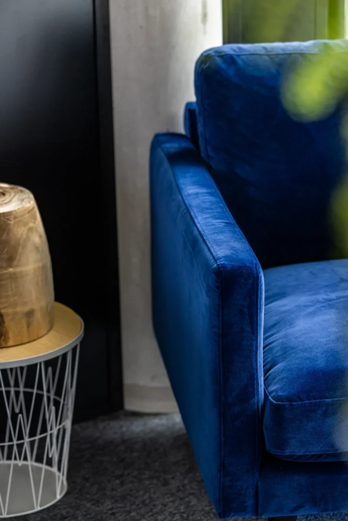 Coin d'un canapé bleu en velours avec une table d'appoint blanche et un objet doré dessus
