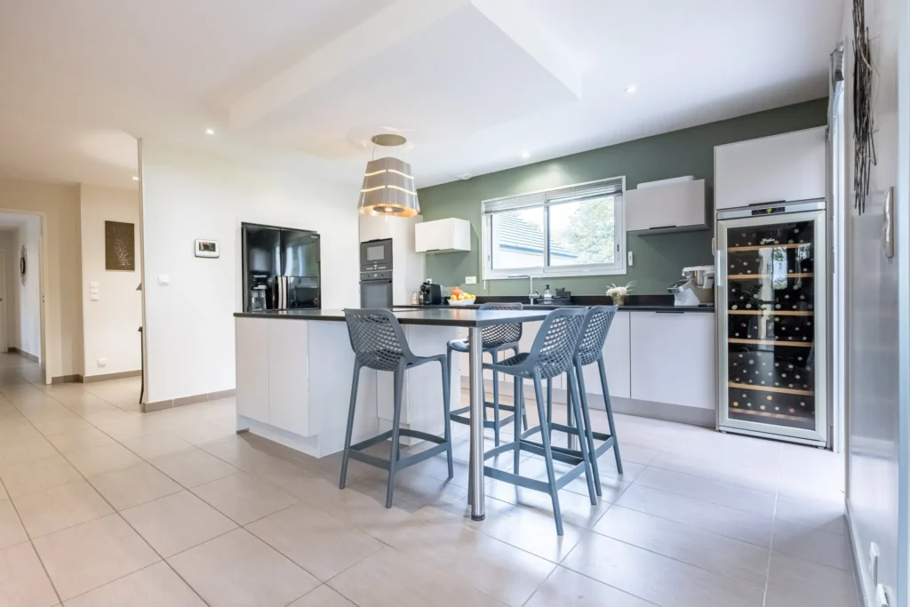 Cuisine moderne avec îlot central, tabourets hauts, électroménagers intégrés et grande fenêtre