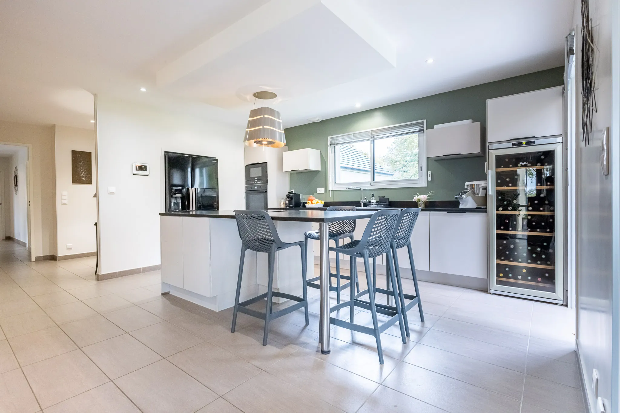 Cuisine moderne avec îlot central, tabourets hauts, électroménagers intégrés et grande fenêtre