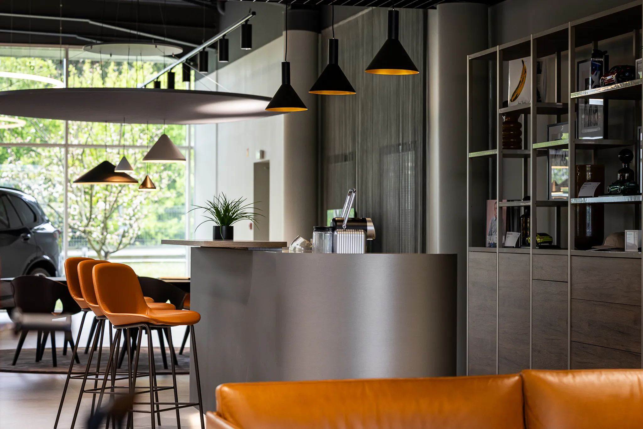 Intérieur moderne avec un bar gris, trois tabourets orange, des suspensions noires, une étagère et un canapé orange au premier plan.