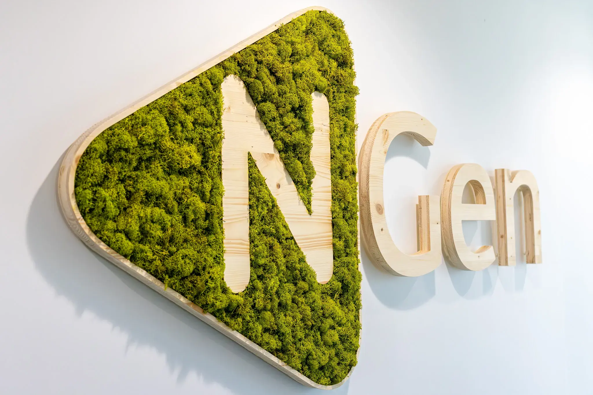 Logo mural avec la lettre N en bois sur fond de mousse verte, suivi des lettres Gen en bois clair sur un mur blanc