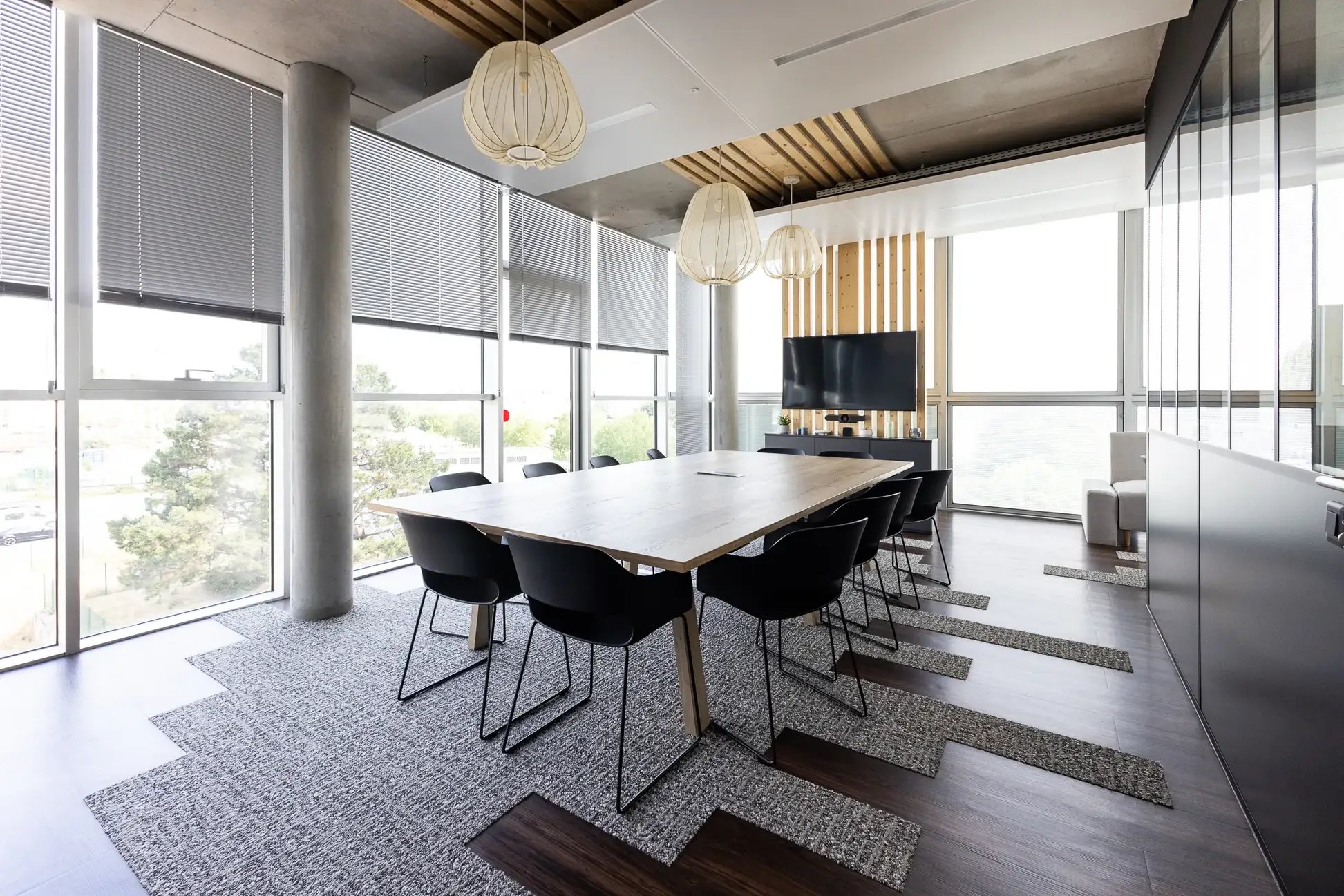 À propos Salle de réunion lumineuse avec grande table en bois, chaises noires, grandes fenêtres et lampes suspendues